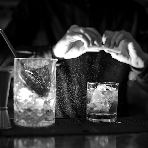 Bartender prepares a cocktail Old Fashioned with ice adding an orange bitter