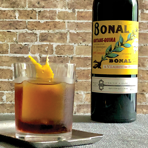 A bottle of Bonal Gentiane-Quina next to a filled glass tumbler with lemon peel garnish