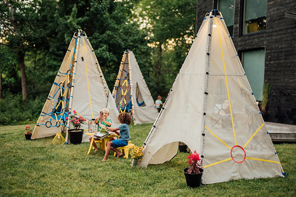 Bijou Build collapsible play structure. The Mainstay Duo Rambler version features two tepee-like structures that can house a swing or lounge pillows with ropes for climbing. Solar-powered LED lights. 