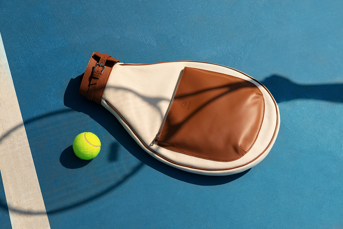 Jurgi Sport Bag on a tennis court next to a tennis ball. This canvas and leather tennis racket bag has room for two rackets, available in three colorways.