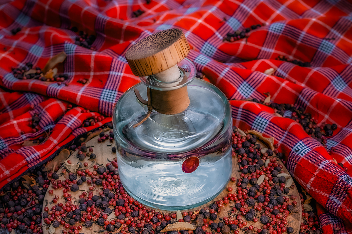 A bottle of Procera Gin on a woodern board surrounded by African juniper berries that provide the vibrant flavor of this distinc spirit crafted for specific cocktails. 