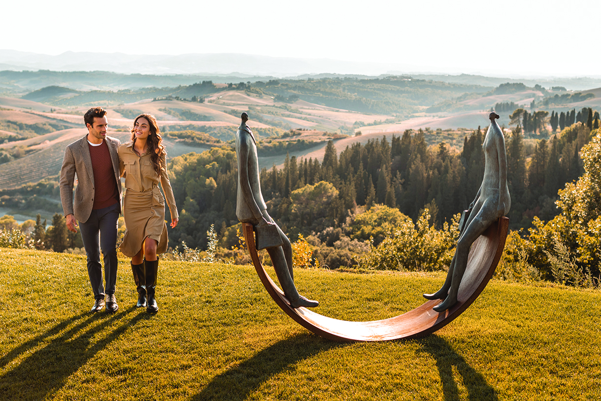 Fashionable couple walking near a garden sculpture in Tuscany.