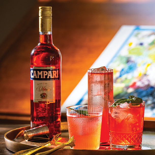 Campari bottle next to three cocktails with mint garnishes on a serving tray