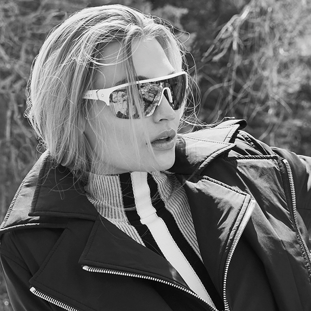 Woman with dark jacket, vertical strip mock neck sweater, and sporty sunglasses