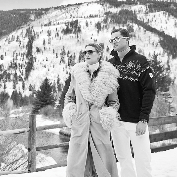 Fashionable couple standing outside near snowy Aspen mountains)