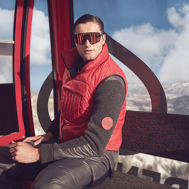 Man wearing red vest with pocket, jacket, ski pants, and polarized, wrapped frame sunglasses
