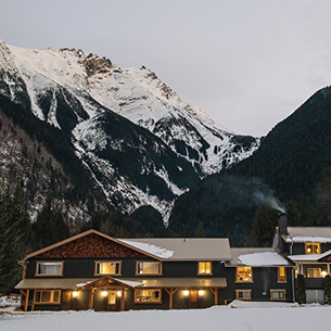 A cozy lodge nestled in a snow, with a majestic mountain towering in the background.