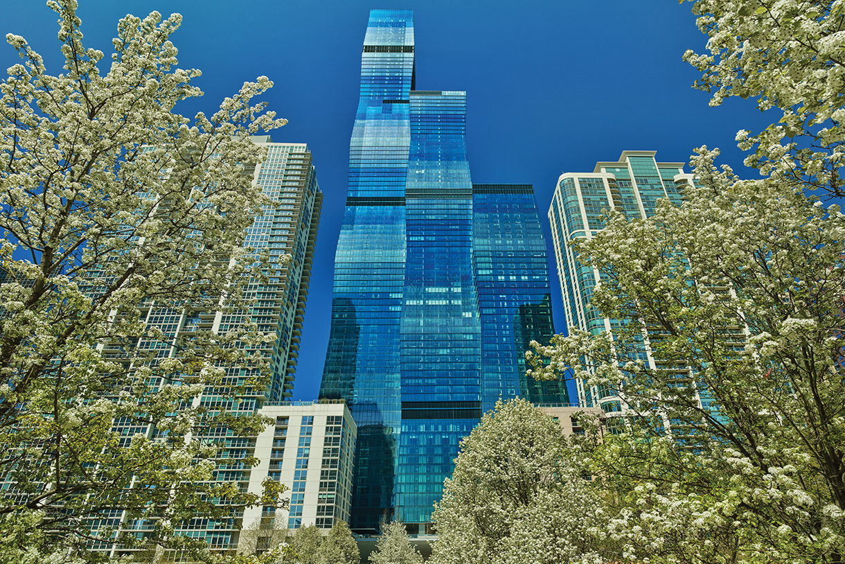 Bottom view of the St. Regis Chicago Hotel surrounded by bright green trees in full bloom.