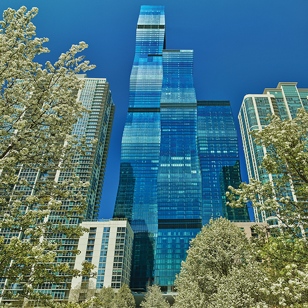 Bottom view of the St. Regis Chicago Hotel surrounded by bright green trees in full bloom.