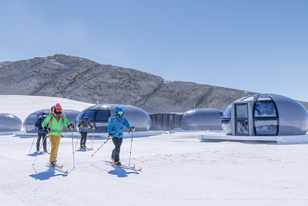 Polar-suited and -booted guests go hiking at Echo Camp. In the background are sky pods and mountains at Antarctica’s uncharted Queen Maud Land.