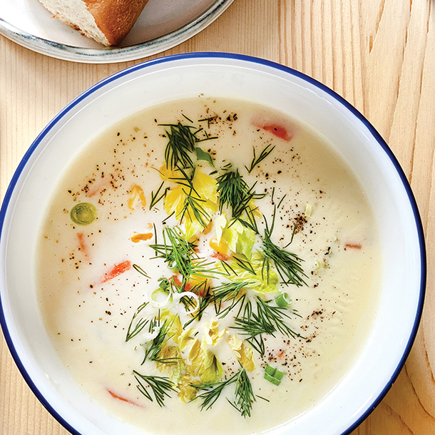 A white bowl with cod and corn chowder, garnished with green dill. The bowl sits on a wooden table.