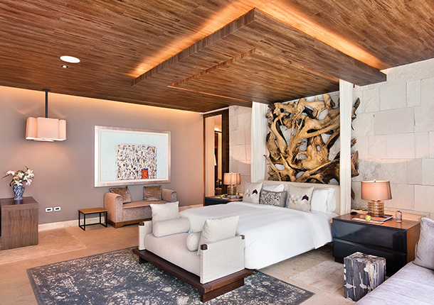 A spacious guest villa with wooden ceiling, wood carved art piece above the bed and stone walls. The space is outfitted with the best of Mexican artisanal design and décor.