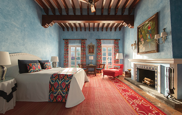  A suite with blue painted walls, wooden beams on the ceiling, a fireplace, two balcony doors and a king-size bed.