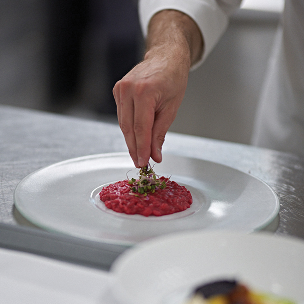 Chef finishing the plate by putting herb garnishes on top of a tomato risotto entrée.