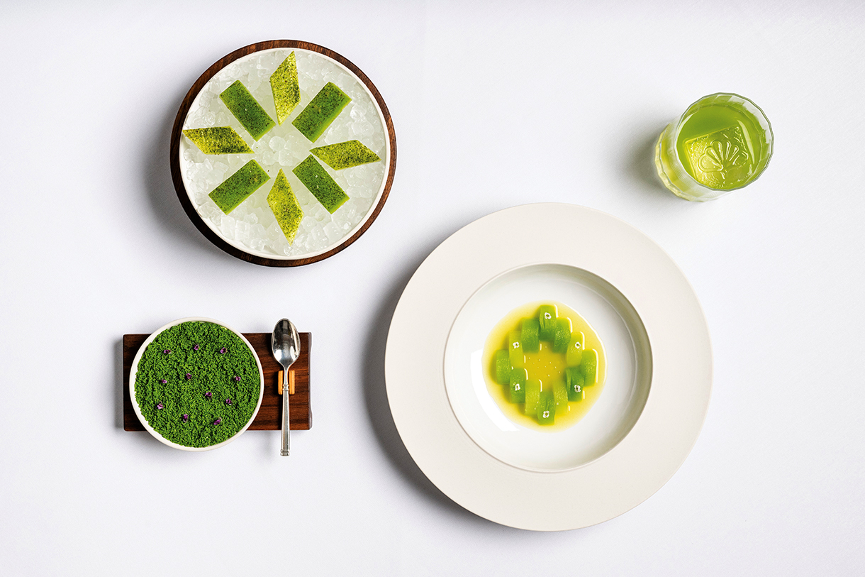 Dishes featuring yellow and green plant-based foods and a glass with a light green drink placed on a white tabletop.