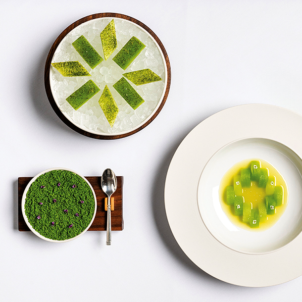 Dishes featuring yellow and green plant-based foods and a glass with a light green drink placed on a white tabletop.)