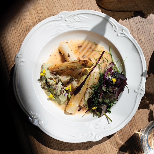 White plate with roasted white asparagus, greens and vegan cream sauce placed on a wooden table.