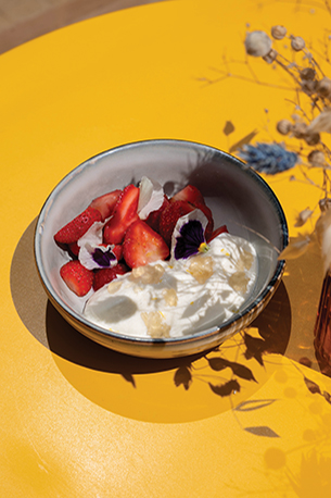 Bowl of strawberries, whipped cream , and sweet clover on a yellow table.