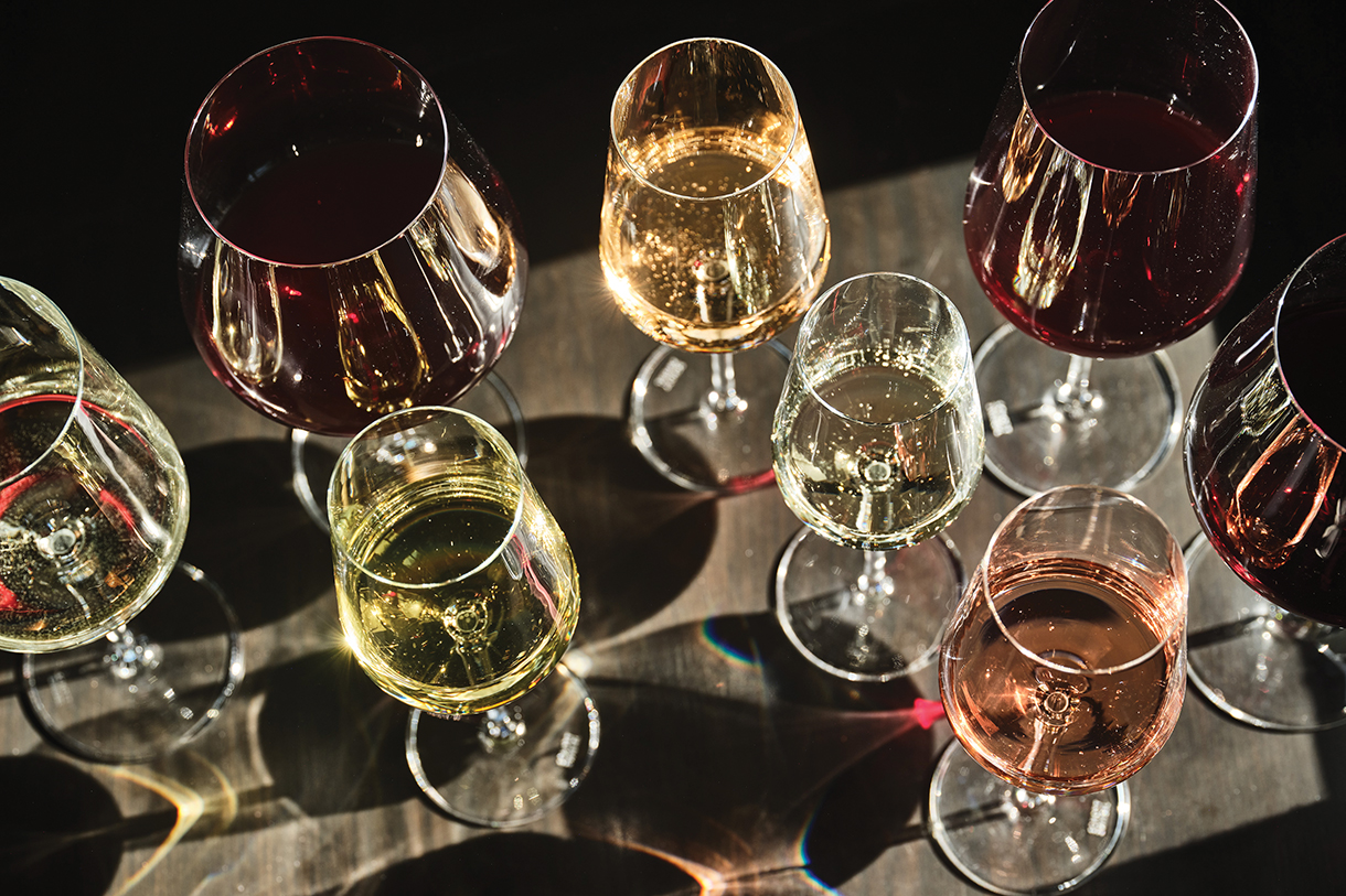 A group of wine glasses filled with different colored wines, sitting on a wooden table.
