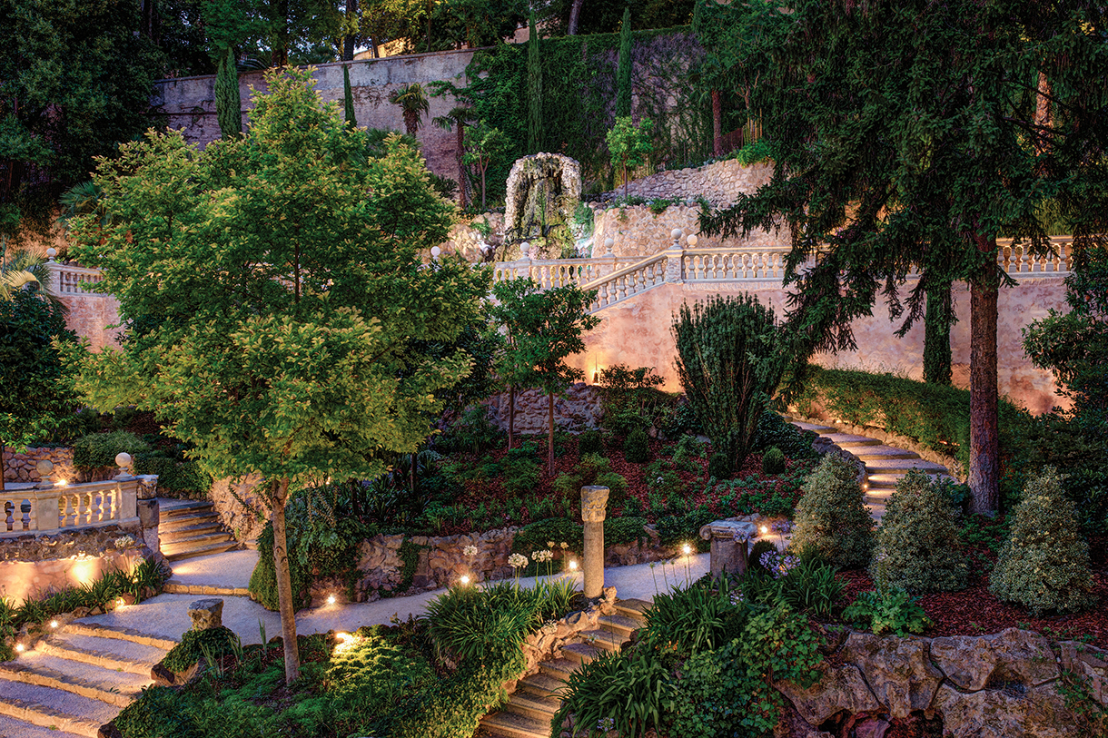 A beautiful lush green garden lit up at night with trees and multiple staircases