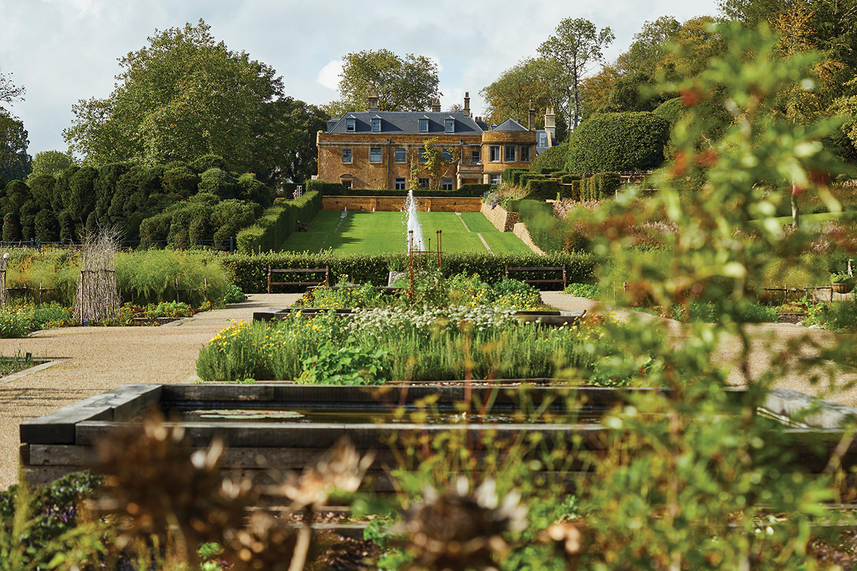 A large formal garden with a with a fountain and country estate in the background
