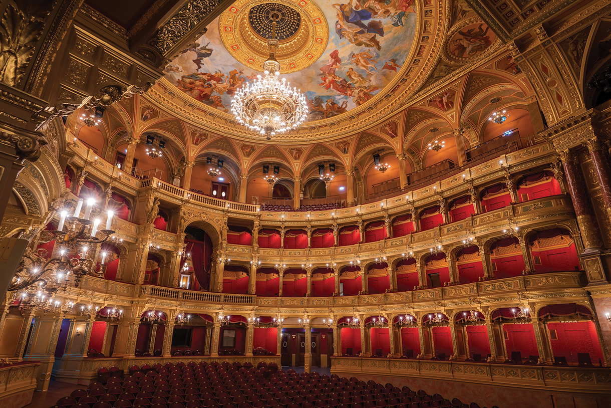 Interior of newly renovated Hungarian 1884 opera house with Old World charms: chandeliers, vaulted ceilings, marble columns, and murals.