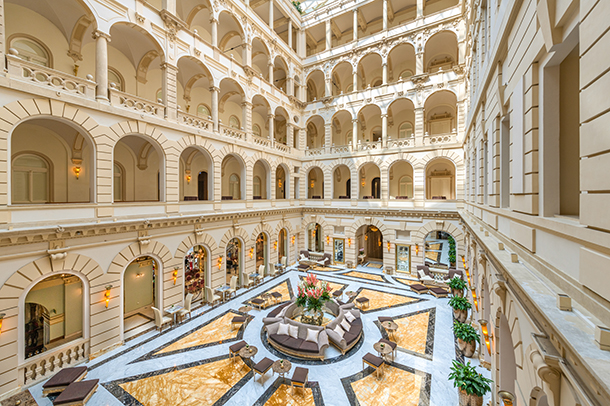 Elegant hotel lobby adorned with lavish decor, featuring marble floors, ornate columns, chandeliers, high ceilings, luxurious furnishings, and intricate architectural details.