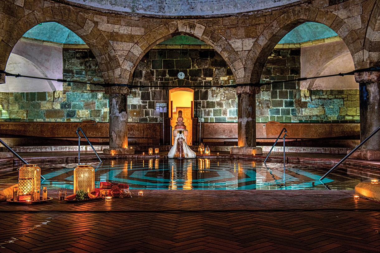 Interior of a historic thermal bath and wellness spa characterized by an octagonal shaped pool covered with red marble and bordered by columns