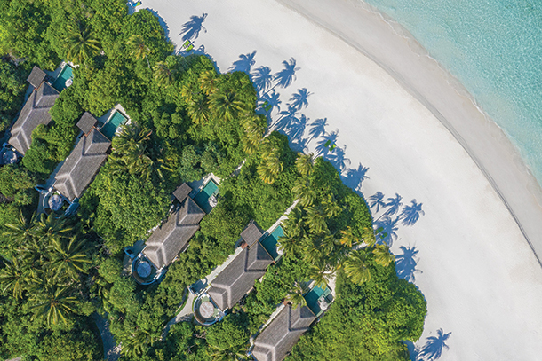 Aerial view of luxurious private resort villas surrounded by palm trees, dense foliage and white sandy beaches.