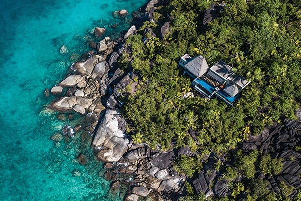 Aerial view of a secluded and luxurious coastal villa with an infinity pool nestled in lush tropical vegetation with stunning views of the turquoise ocean.