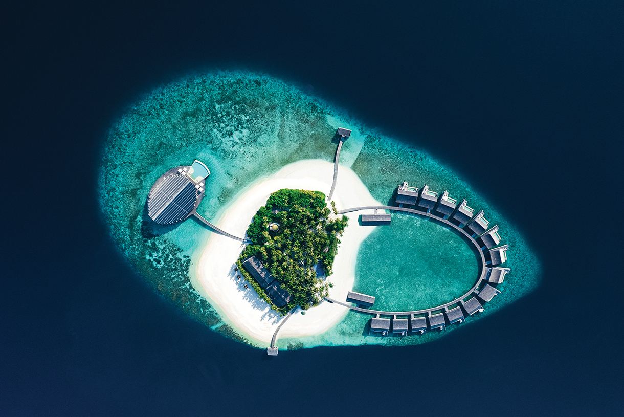 Aerial view of secluded and luxurious Kudadoo Maldives Private Island surrounded by coral reefs and deep blue ocean waters