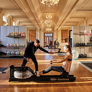 Woman receiving personal strength training from instructor on water rowing machine