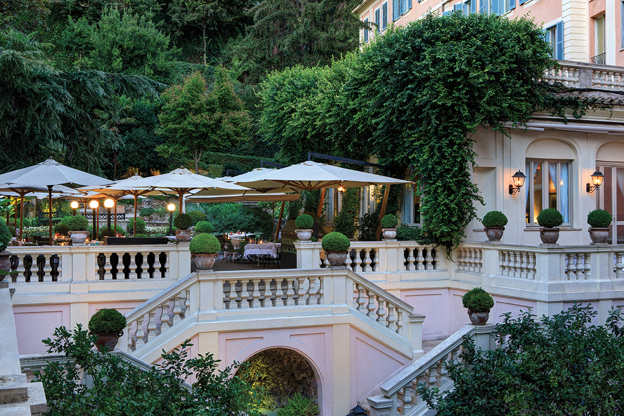 Outdoor patio of hotel with double staircase surrounded by beautiful lush garden