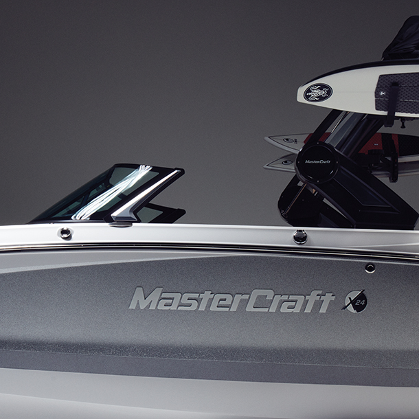 Side view of a silver and white MasterCraft X24 wakesurf boat holding Connelly wakeboards