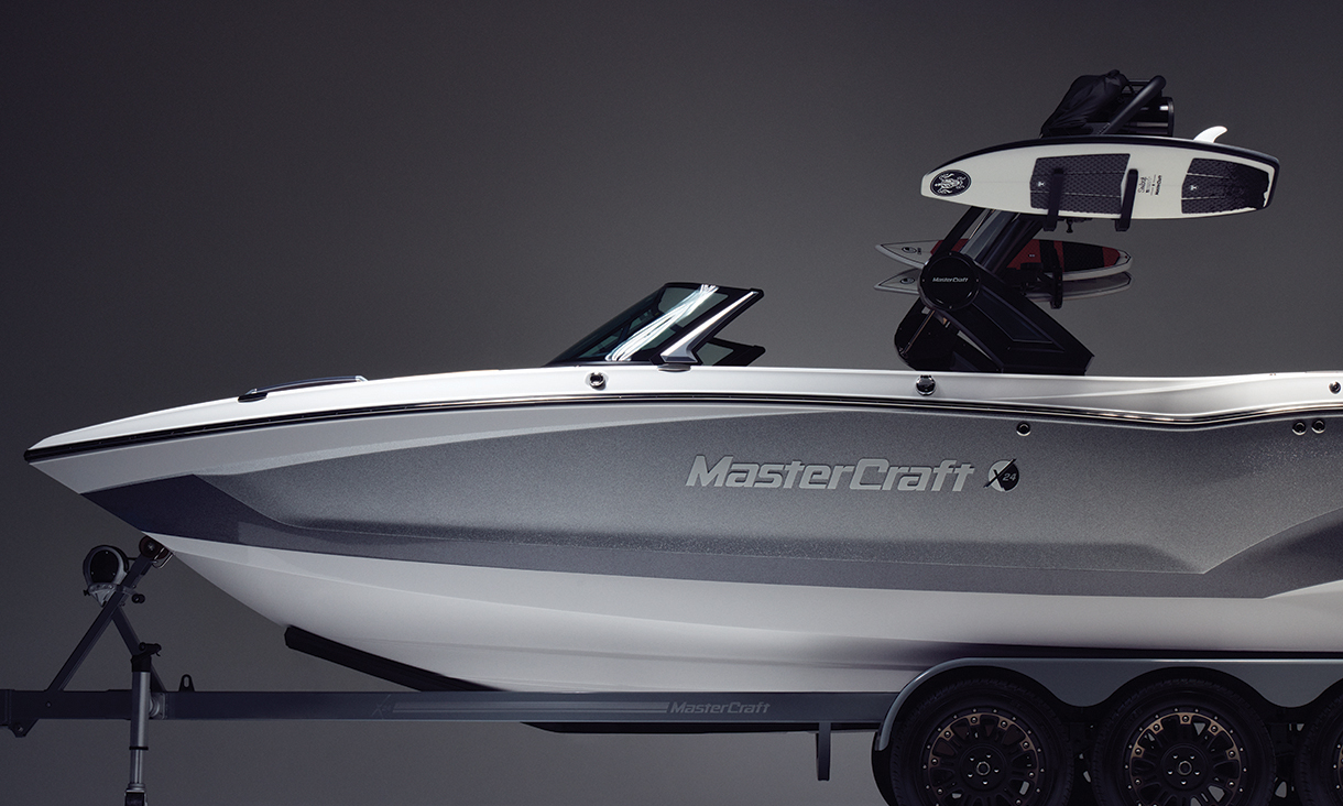 Side view of a silver and white MasterCraft X24 wakesurf boat holding Connelly wakeboards 