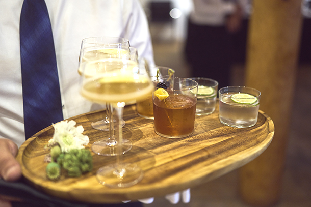 Closeup of server serving alcohol beverages with garnishes on a wooden tray