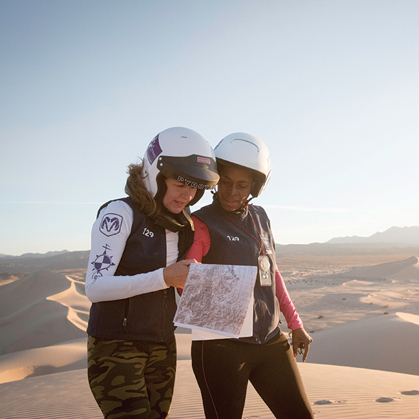 Two women wearing racing helmets look at map to compete in off-road rally