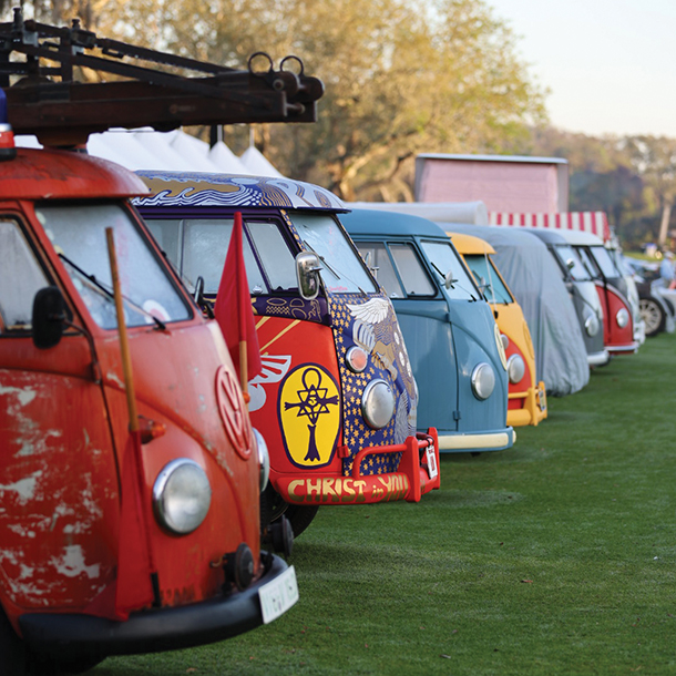 olorful VW vans lined up on display at a car show on a golf green.