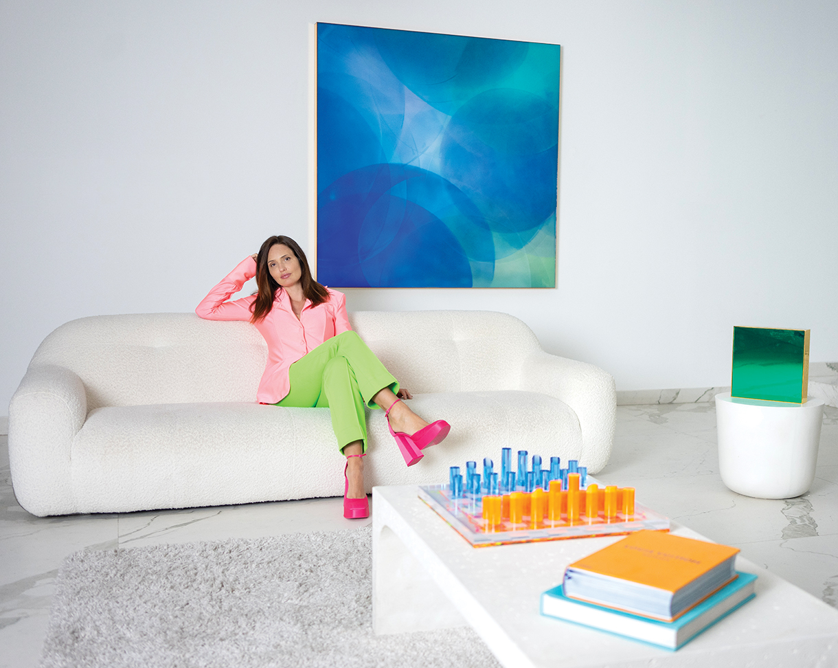 Artist Nat Bowen sitting on a white couch in front of Big Blue art piece mounted on a white wall 
