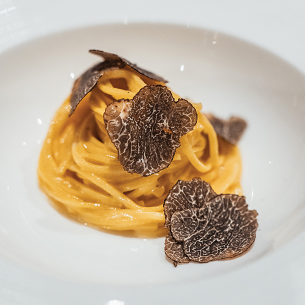  A plate of tagliolini pasta topped with shaved black truffles. The pasta is a rich golden color, and the truffles are dark and earthy.