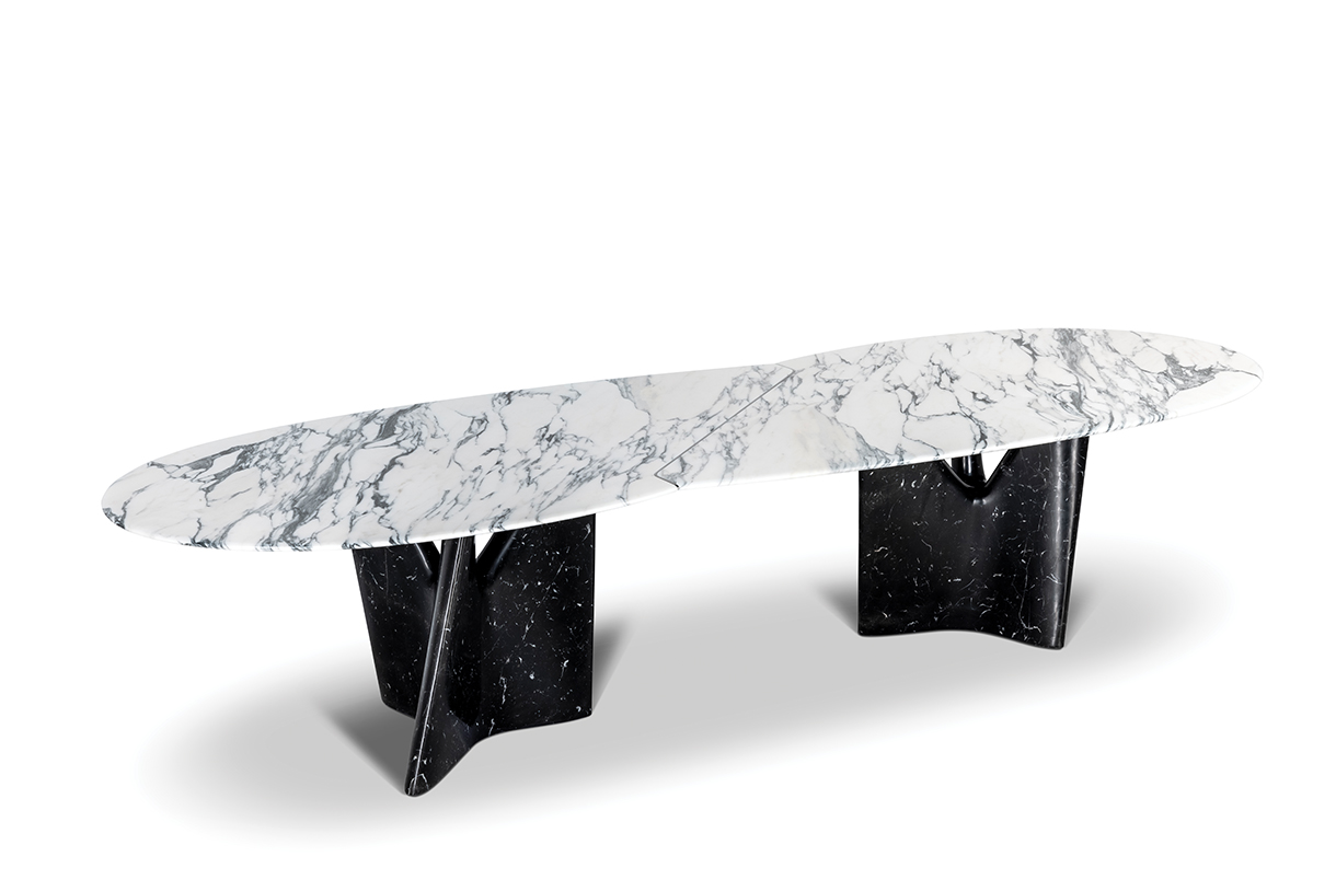 A long, oval dining table with a white marble top and a black marble base. The base has a unique, geometric shape with four legs that intersect in the center.