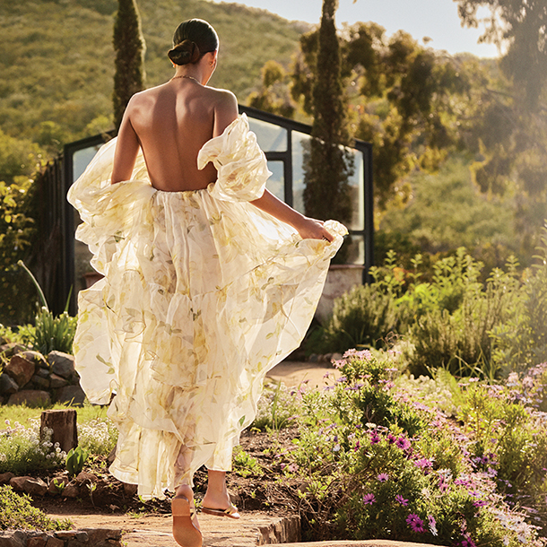 Woman wearing flowy white floral dress walking in botanical garden. 