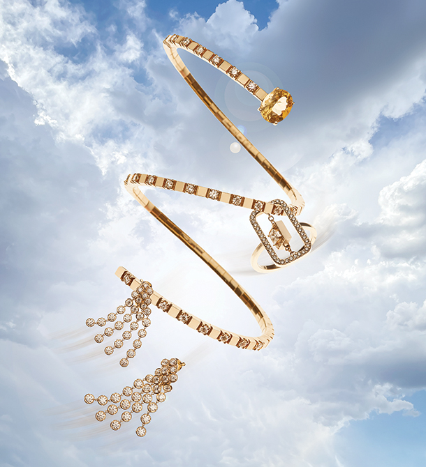 Diamond and gold spiral bracelet with diamonds and beryl, a gold chain ring with princess cut center and a pair of diamond chain earrings suspended in a sky background.