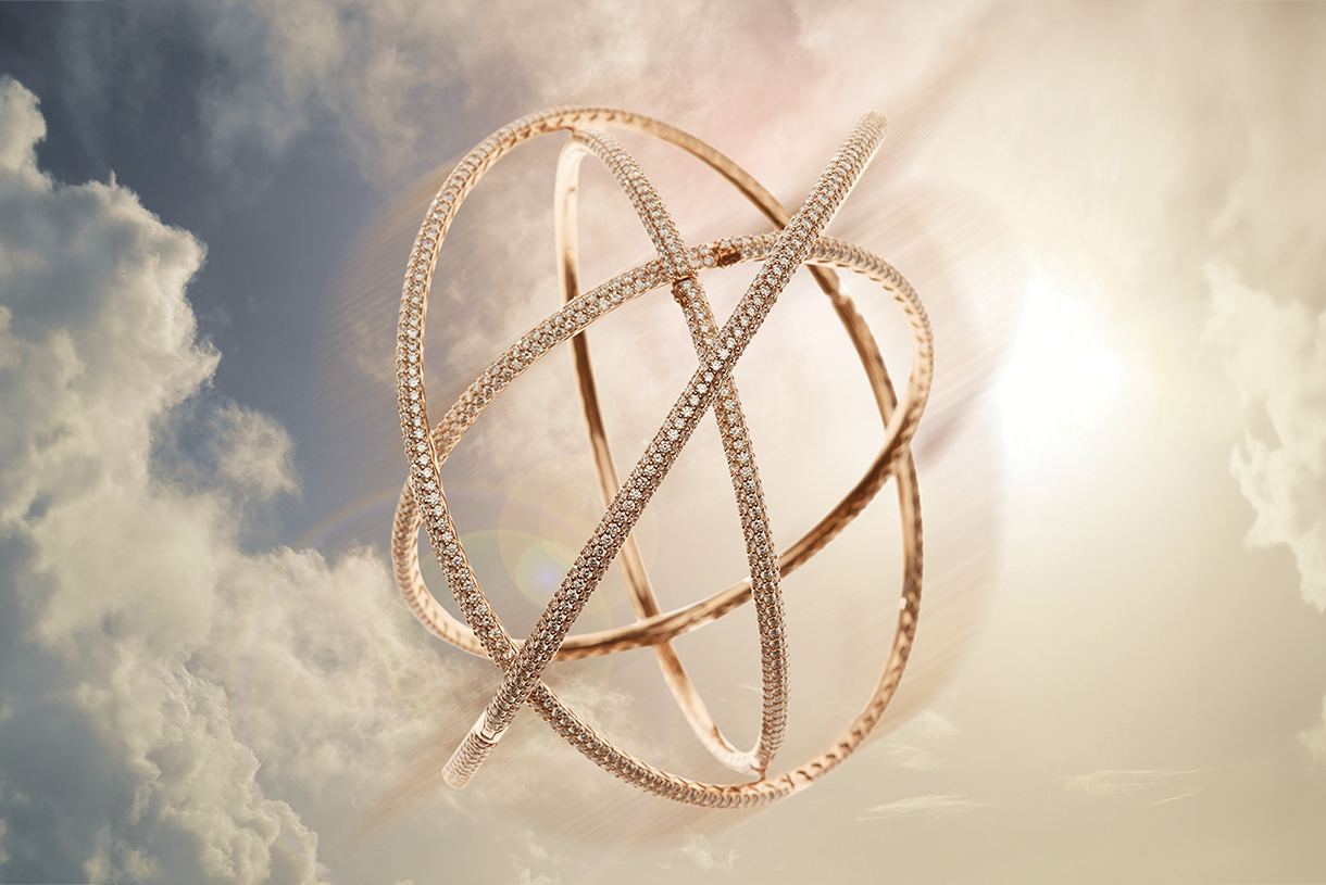 Beautiful diamond and gold bracelets arranged in a spherical shape floating the air in front of a cloudy sky backdrop.