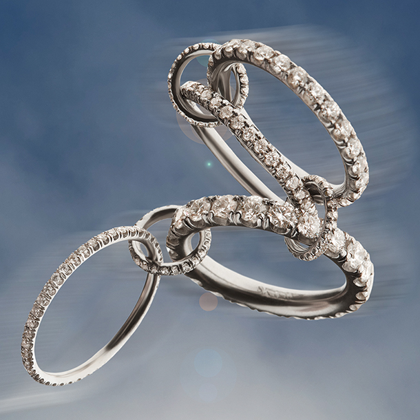 A gorgeous display of platinum pave rings and connectors, each component of the ring is studded with white diamonds that reflect light in a stunning array with a blue sky background. 