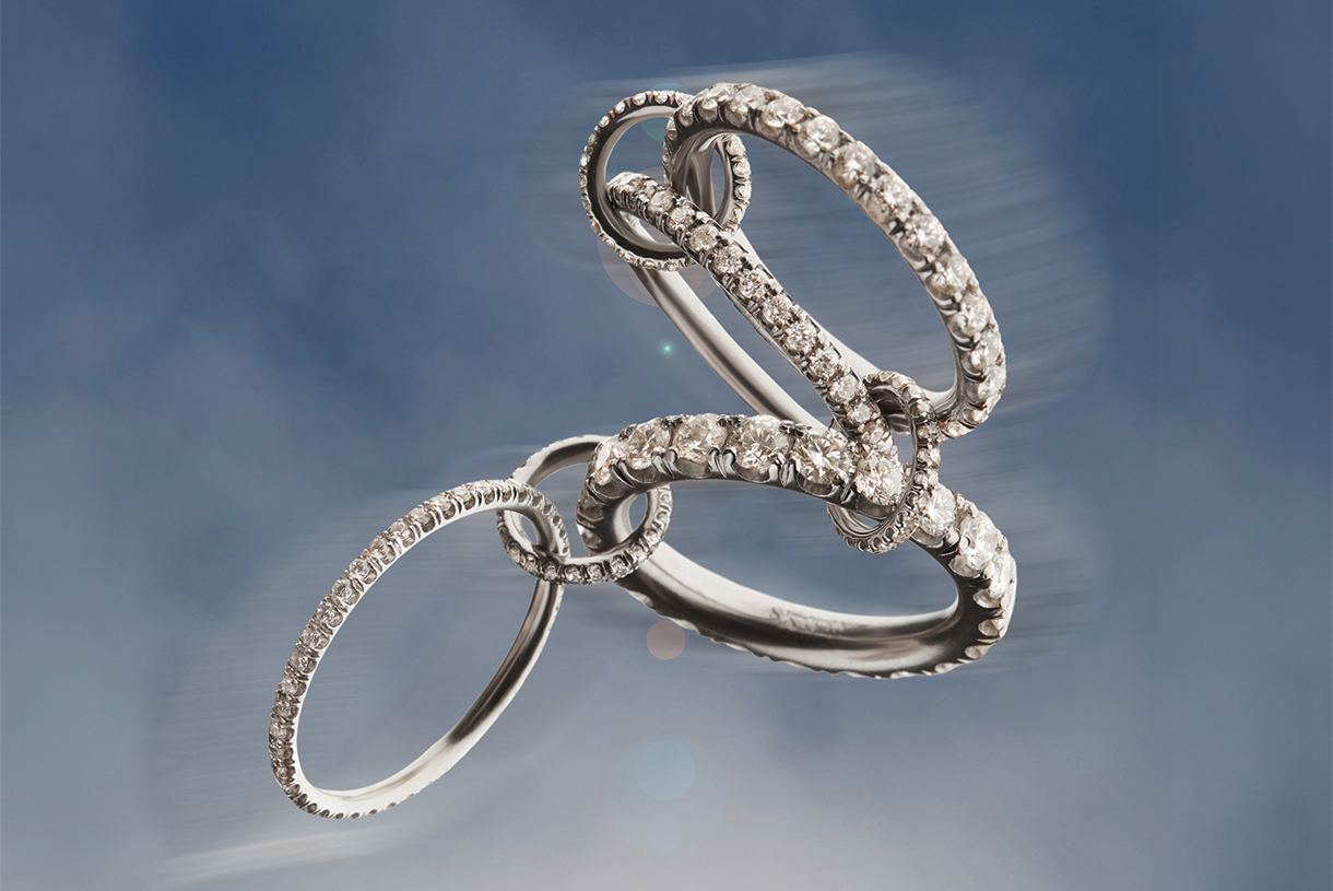 A gorgeous display of platinum pave rings and connectors, each component of the ring is studded with white diamonds that reflect light in a stunning array with a blue sky background.