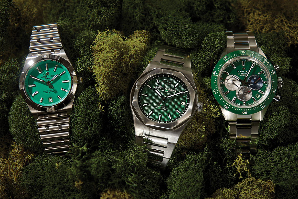 Three watches with green dials and steel bands sitting on top of green moss.