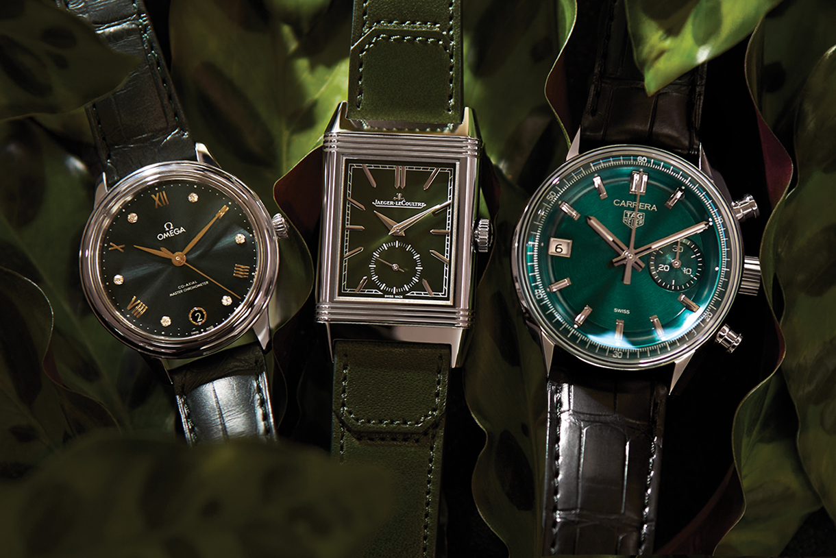 Three classic luxury watches with green dials and leather bands sitting on green leaves.