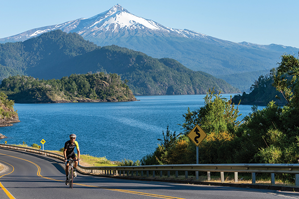 A person riding a bicycle on a winding paved road on the coast of Chile. There are mountains in the distance.