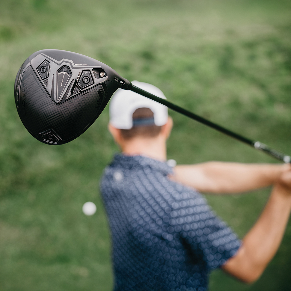 A male golfer hitting a golf ball with a black Cobra Darkspeed LS driver. There is a close-up view of the performance golf club head.